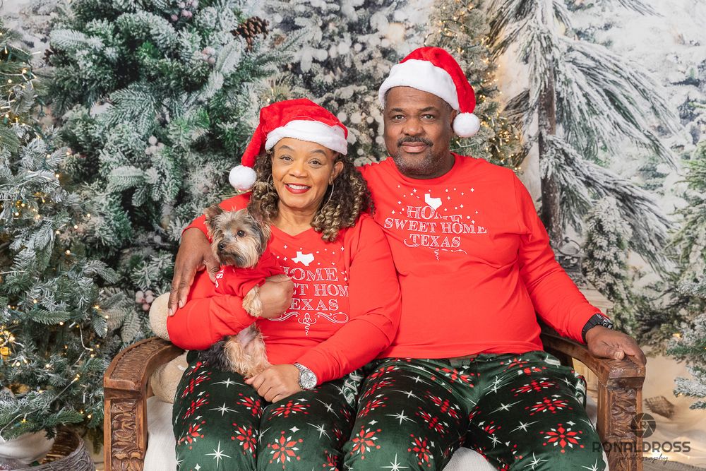 People wearing matching red Christmas sweaters pose together in front of snow-covered evergreen trees during winter. Holiday Photos Webster