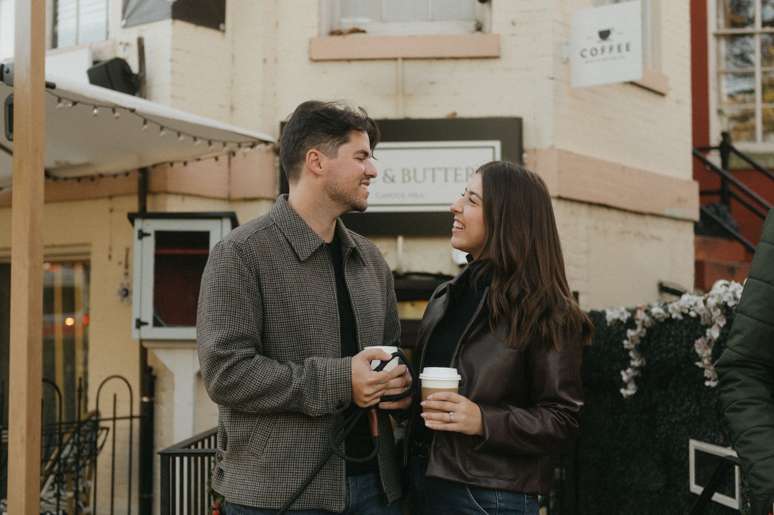 A couple in warm coats shares coffee and conversation while walking down a charming city street.