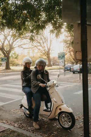 A white Vespa scooter parked on a tree-lined street during fall.