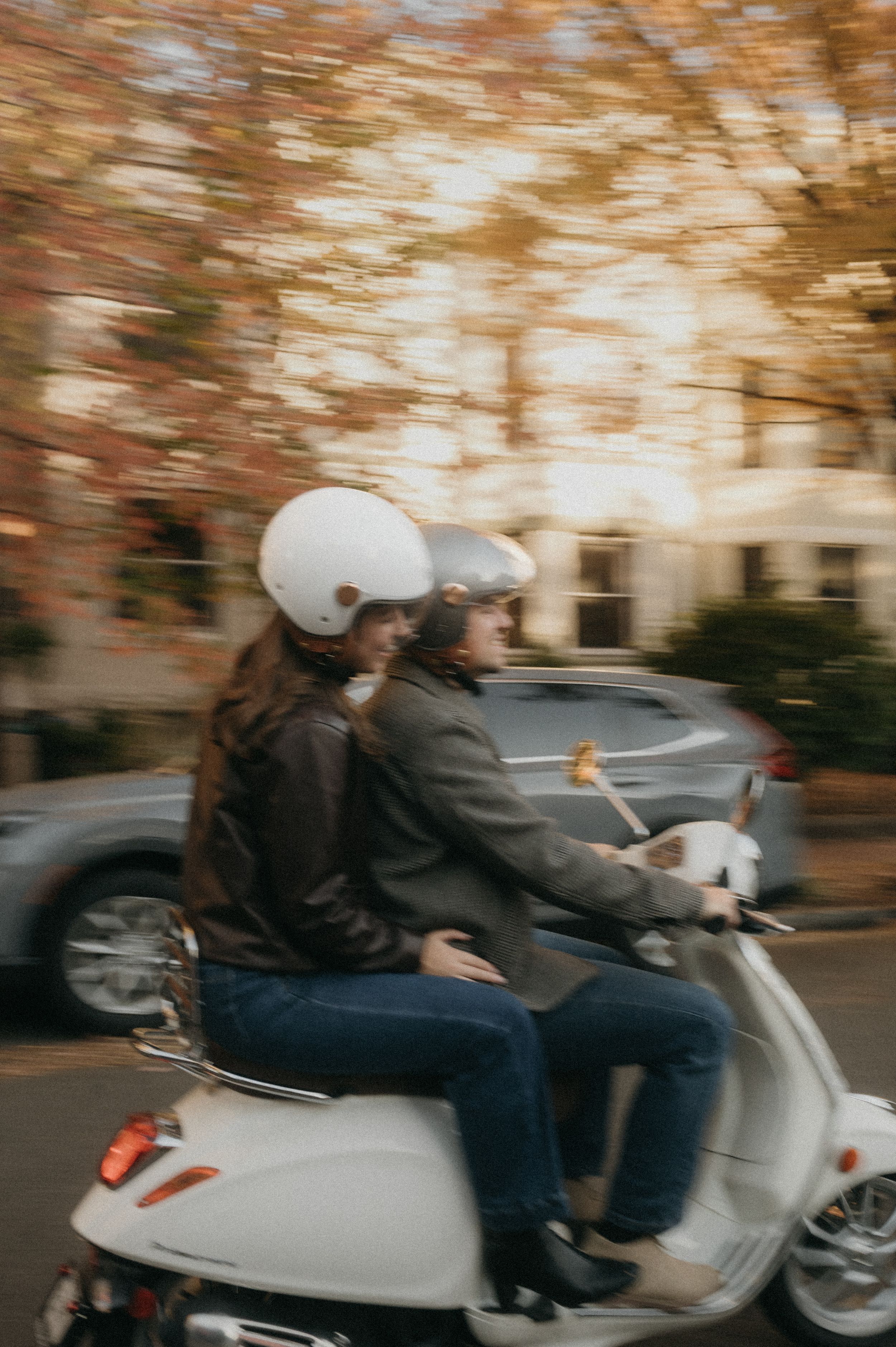 Motion blur captures a silver scooter speeding past autumn trees on a residential street.