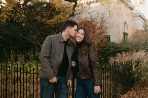 A couple shares an intimate moment in a park during golden hour with autumn foliage in the background.