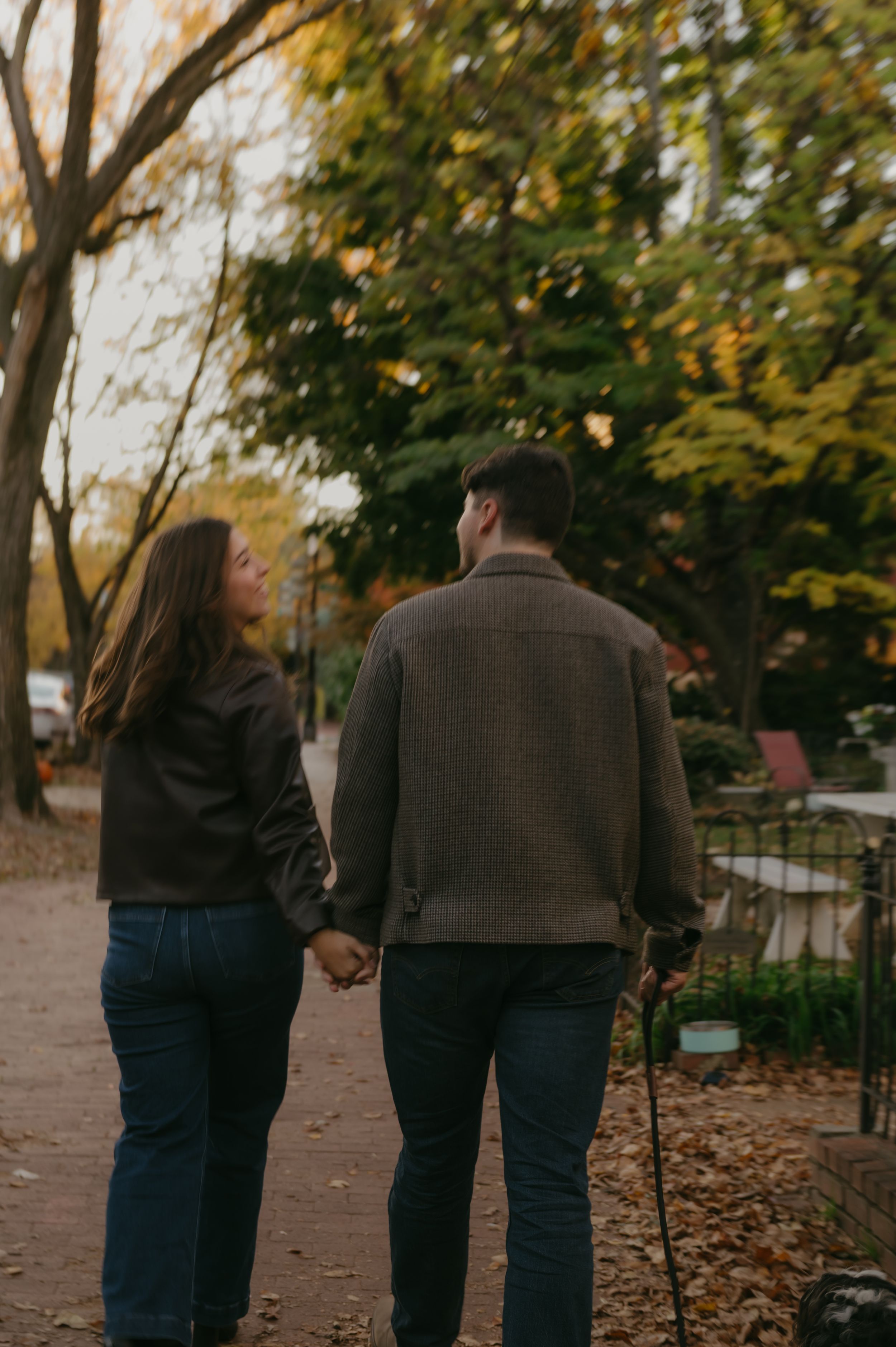 A couple walking together on a path surrounded by autumn trees and fallen leaves.