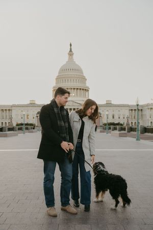A couple walks their black dog on the plaza in front of the US Capitol building.