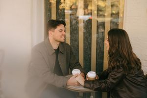 A couple sits together at a cafe table sharing coffee and conversation in a warm indoor setting.