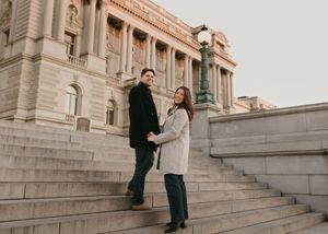 Two people stand on grand stone steps of a historic building having a conversation.