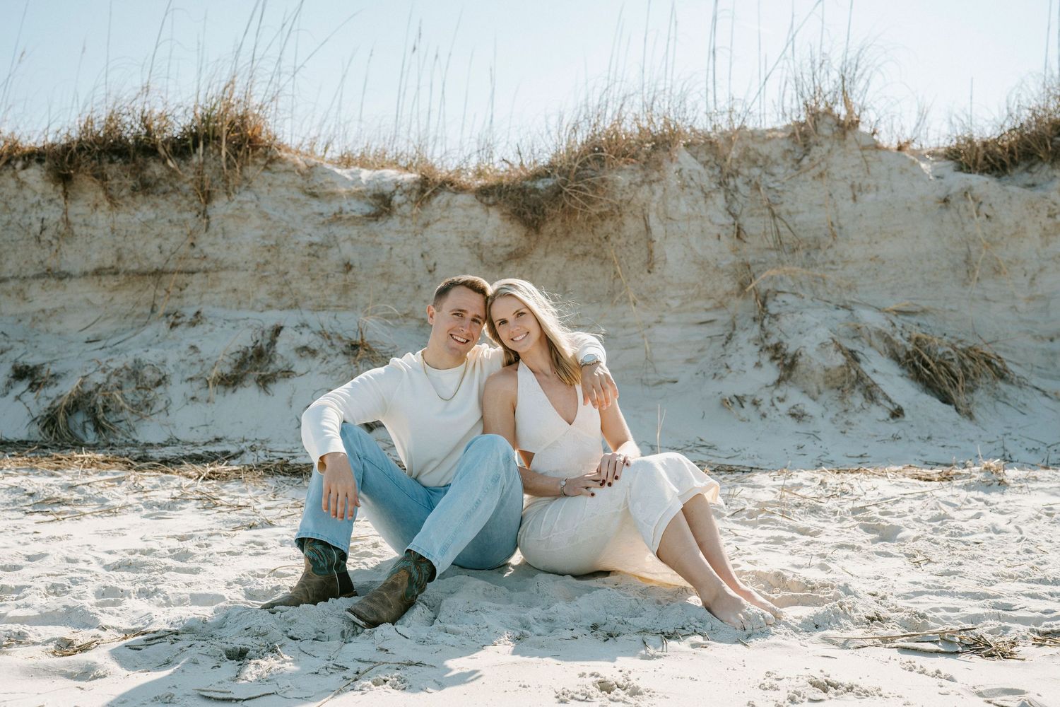 A romantic couple relaxes together on a sandy beach against white cliffs on a sunny afternoon.