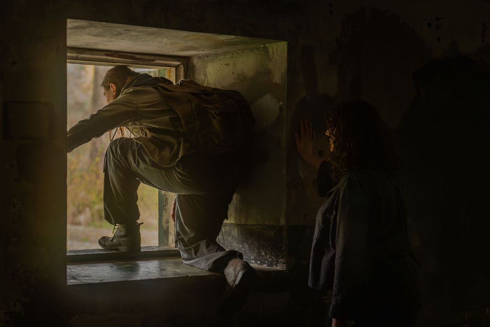 A sequence of dark silhouettes peering through a window in a dimly lit space creates an eerie atmosphere.