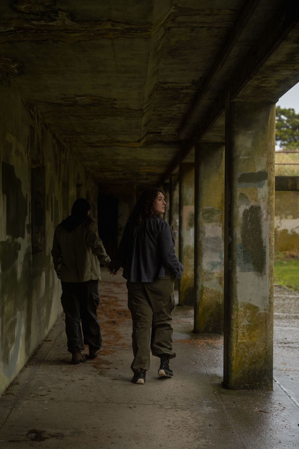 A person walks through a dimly lit concrete tunnel with pillars casting shadows on the ground.