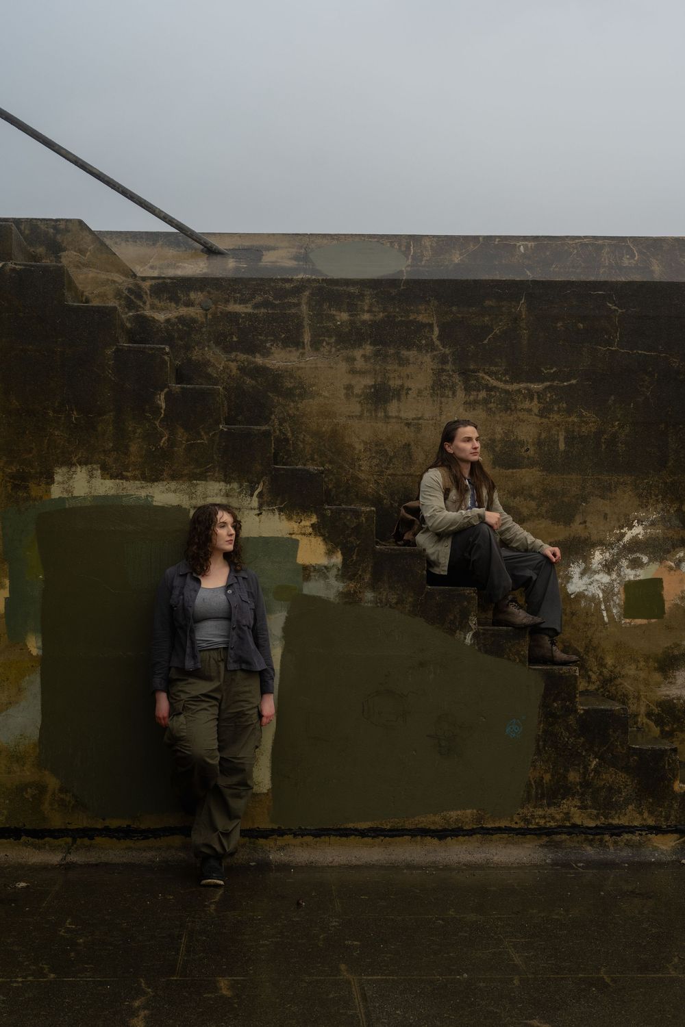 Two people pose dramatically against a dark stone wall in an artistic photo sequence.