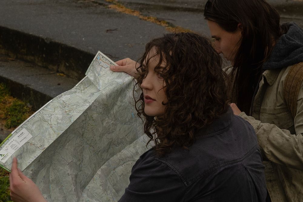 A person reads a large paper map while walking outdoors in an urban area.