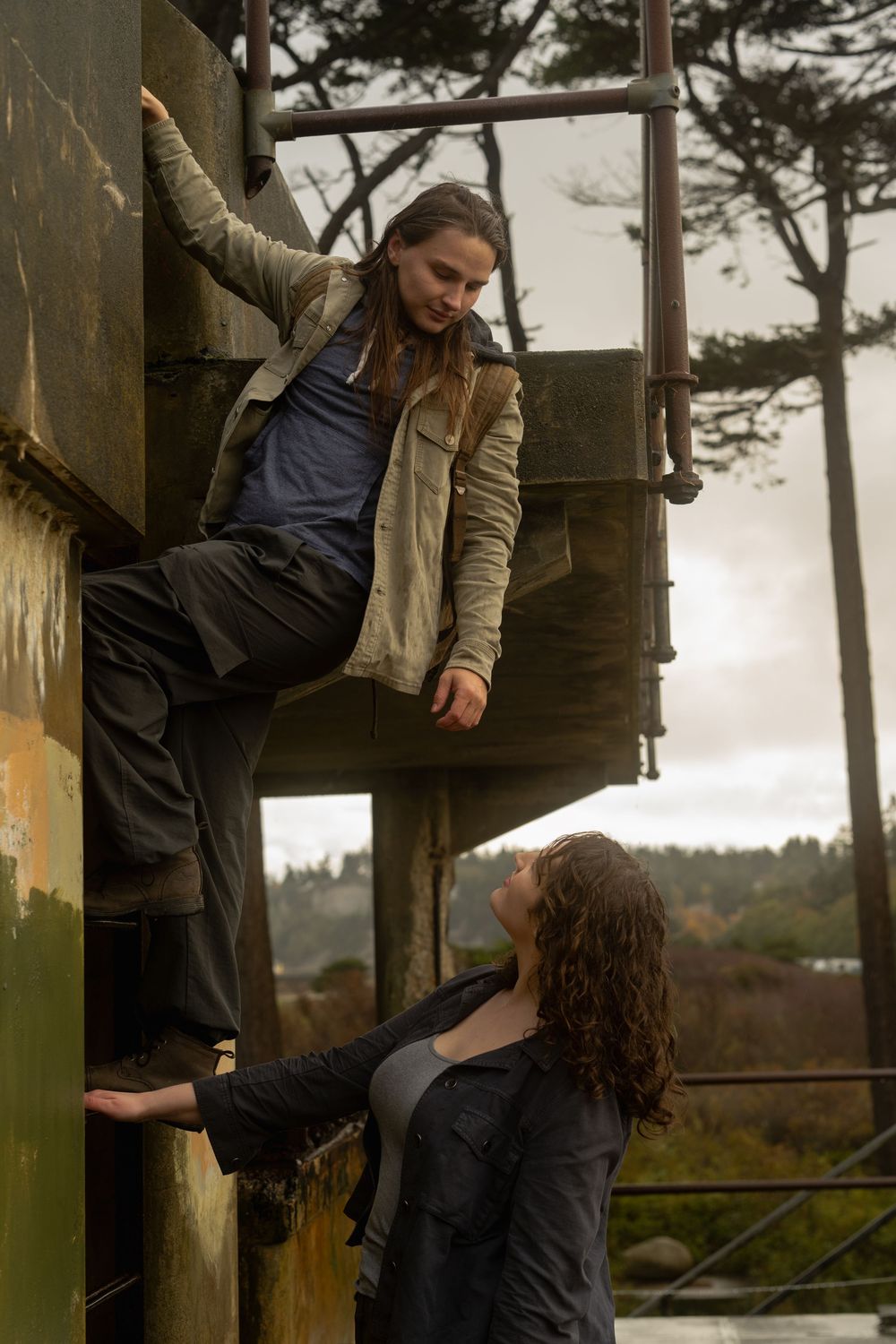A couple performs a dance lift sequence against a moody coastal backdrop with pine trees.