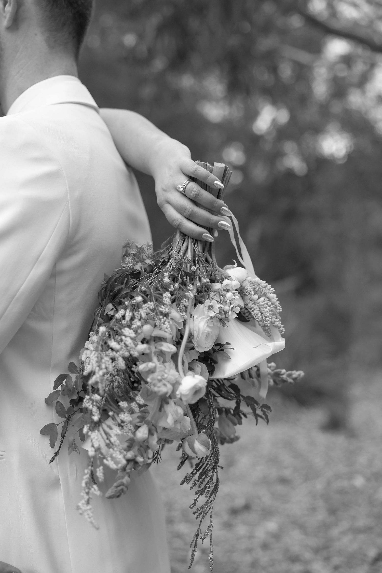 Black and white photo of a bride’s bouquet held close, highlighting her ring and the romantic elegance of the moment.