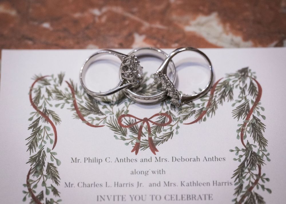 Wedding rings displayed on an elegant invitation with evergreen branch decorations.