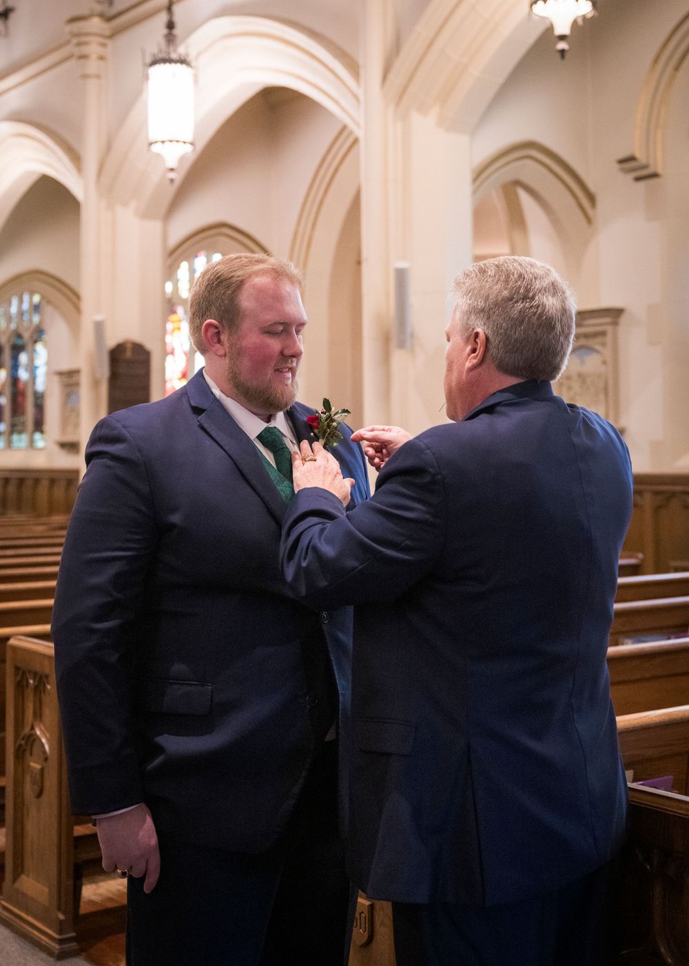 Two people adjusting a boutonniere in a church with arched ceilings.