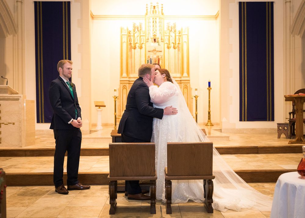 A wedding ceremony taking place at the altar of an elegant church with a grand chandelier.