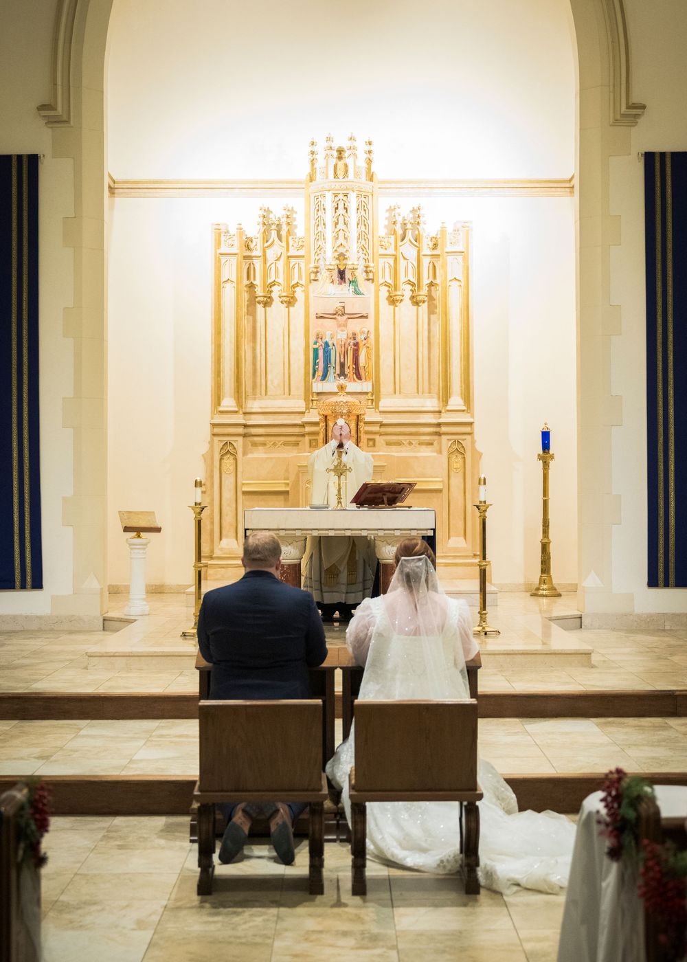 A couple seated at the altar during their wedding ceremony beneath an ornate golden backdrop.