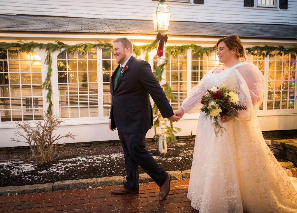 A couple walks together during their winter wedding celebration with twinkling lights and greenery decorations.