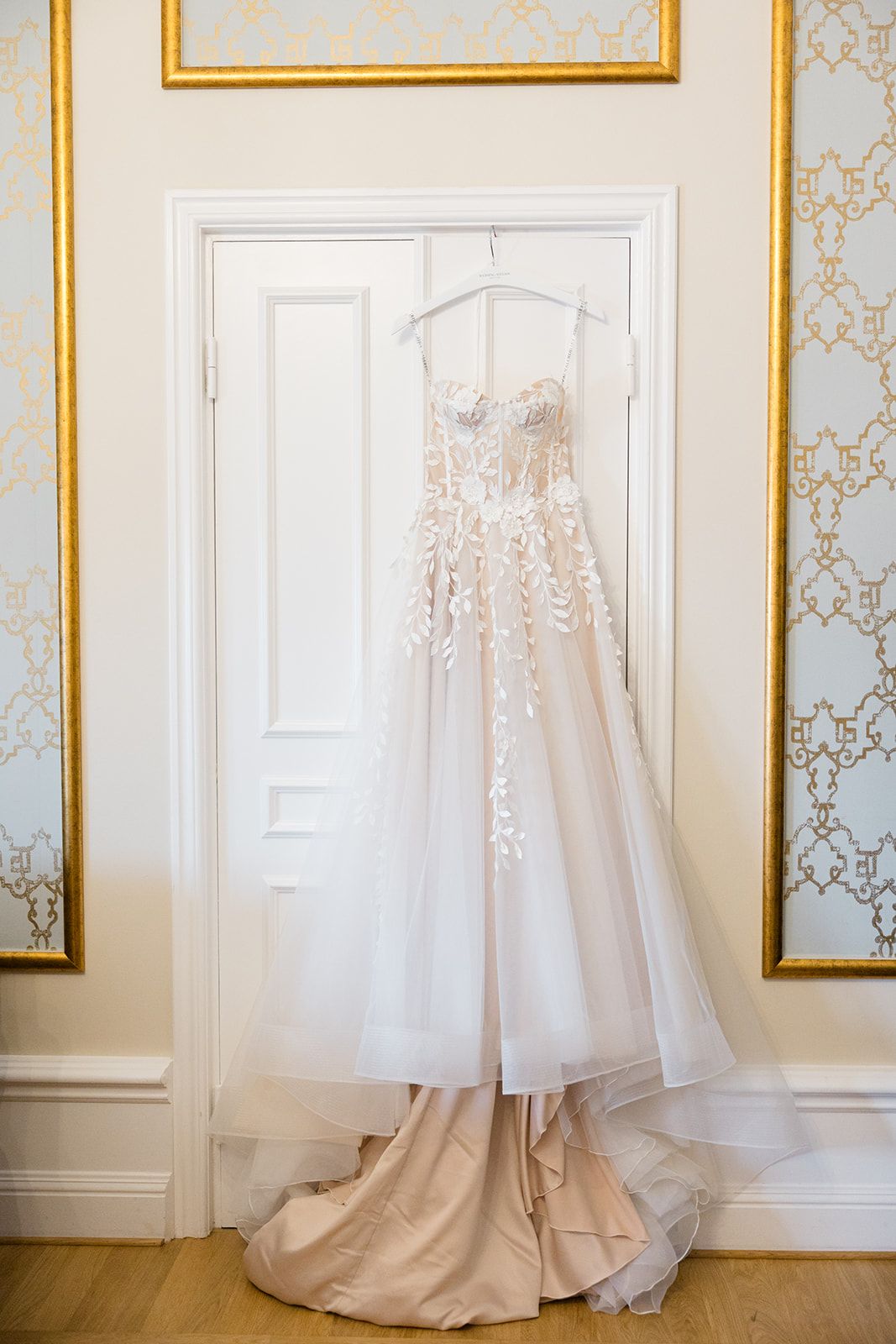A series of elegant white wedding dresses displayed against a light blue and gold wallpapered wall in a bridal boutique.