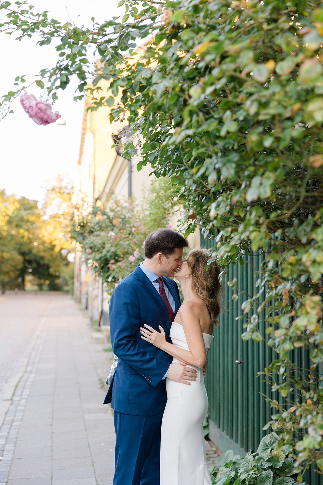 Romantic wedding couple shares intimate moments in a garden setting with green foliage and sunlit pathway.