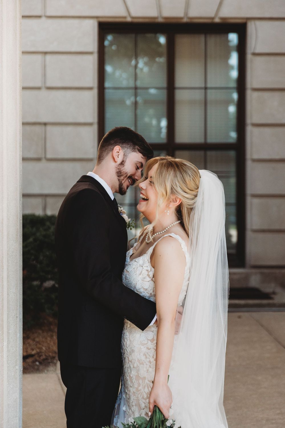 A romantic wedding portrait of a couple sharing an intimate moment against a stone building backdrop.