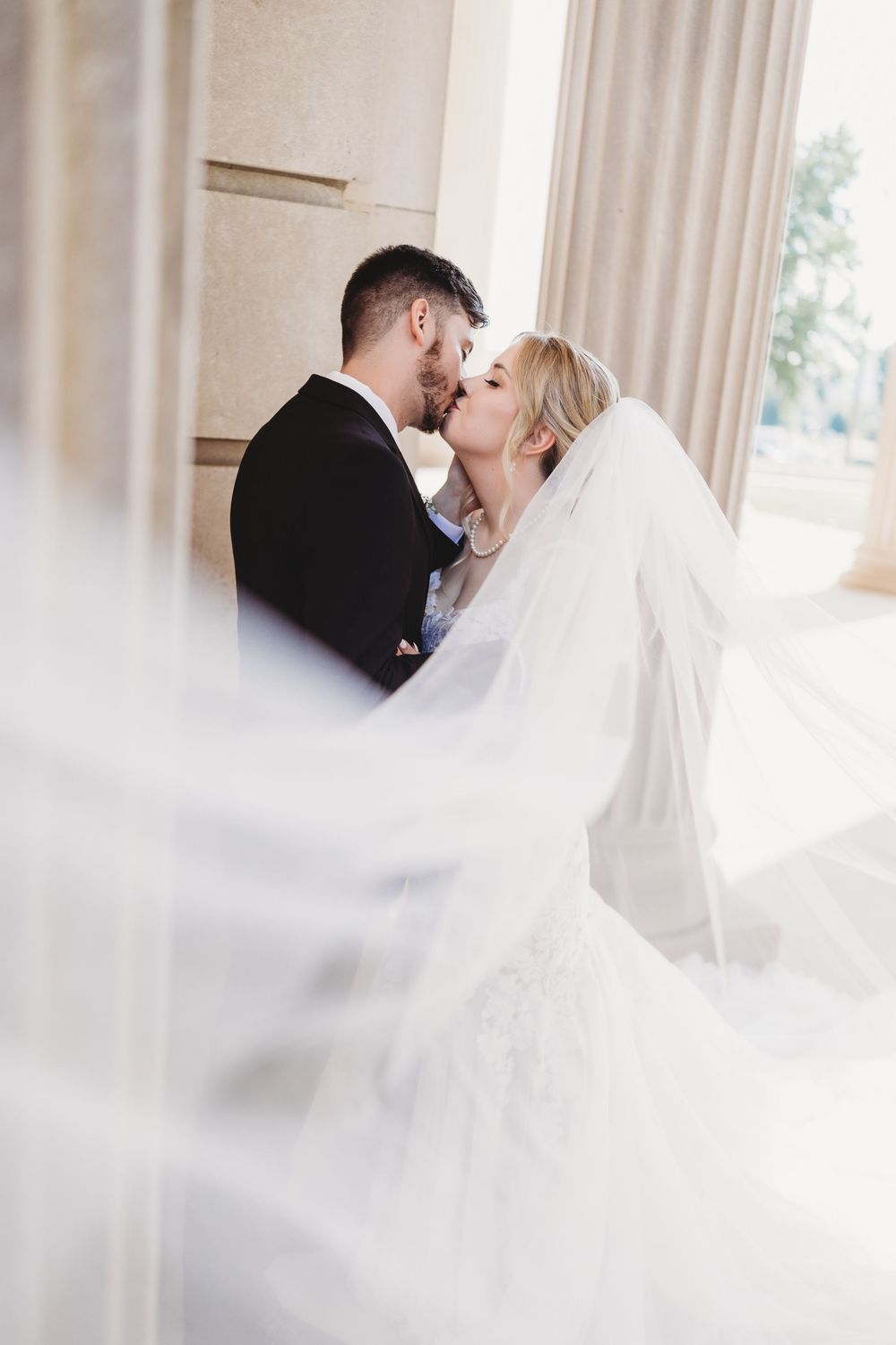 A dreamy wedding portrait with flowing veil creating an ethereal effect in soft natural light.