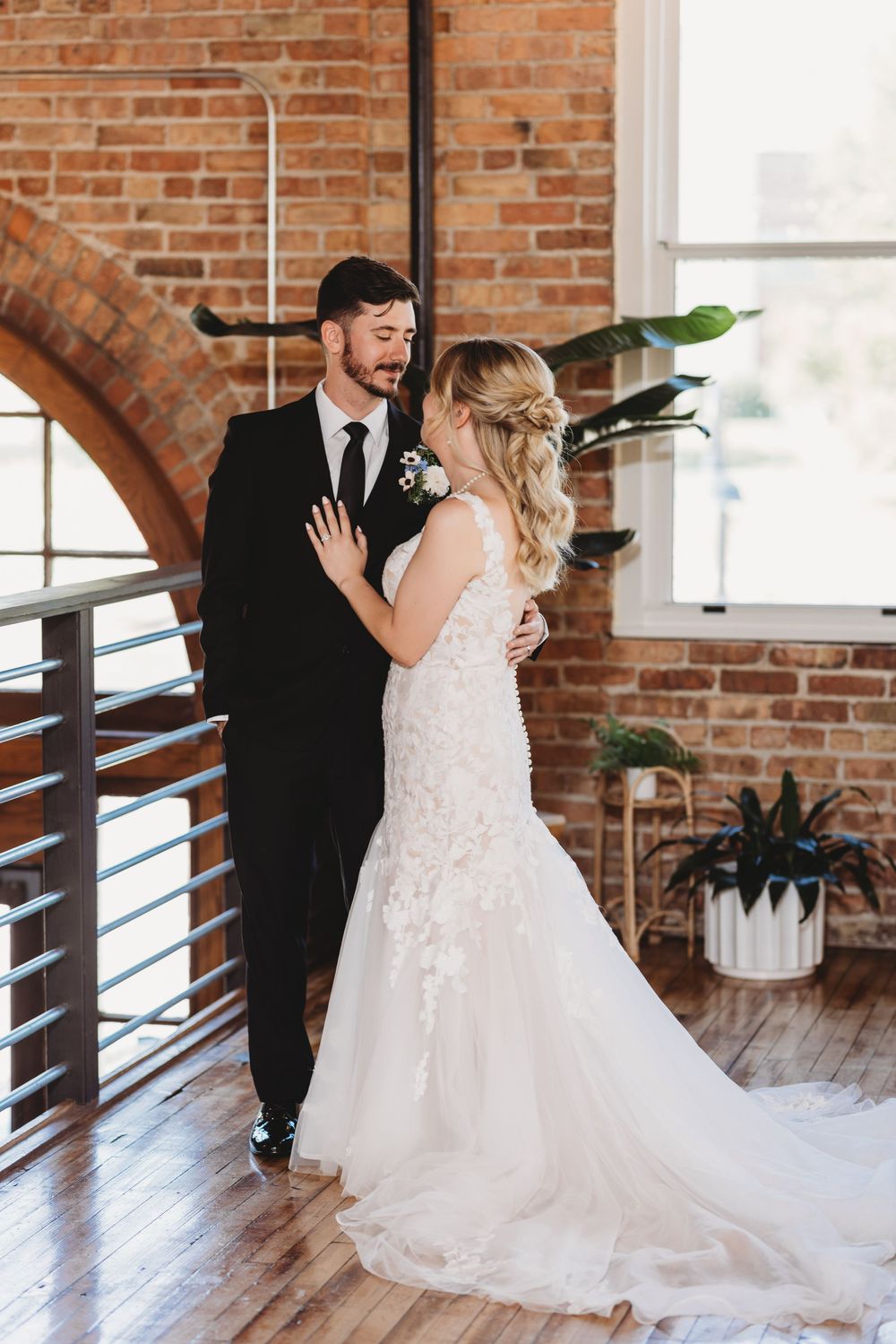A couple shares an intimate moment in a rustic brick venue with large windows and wooden floors.