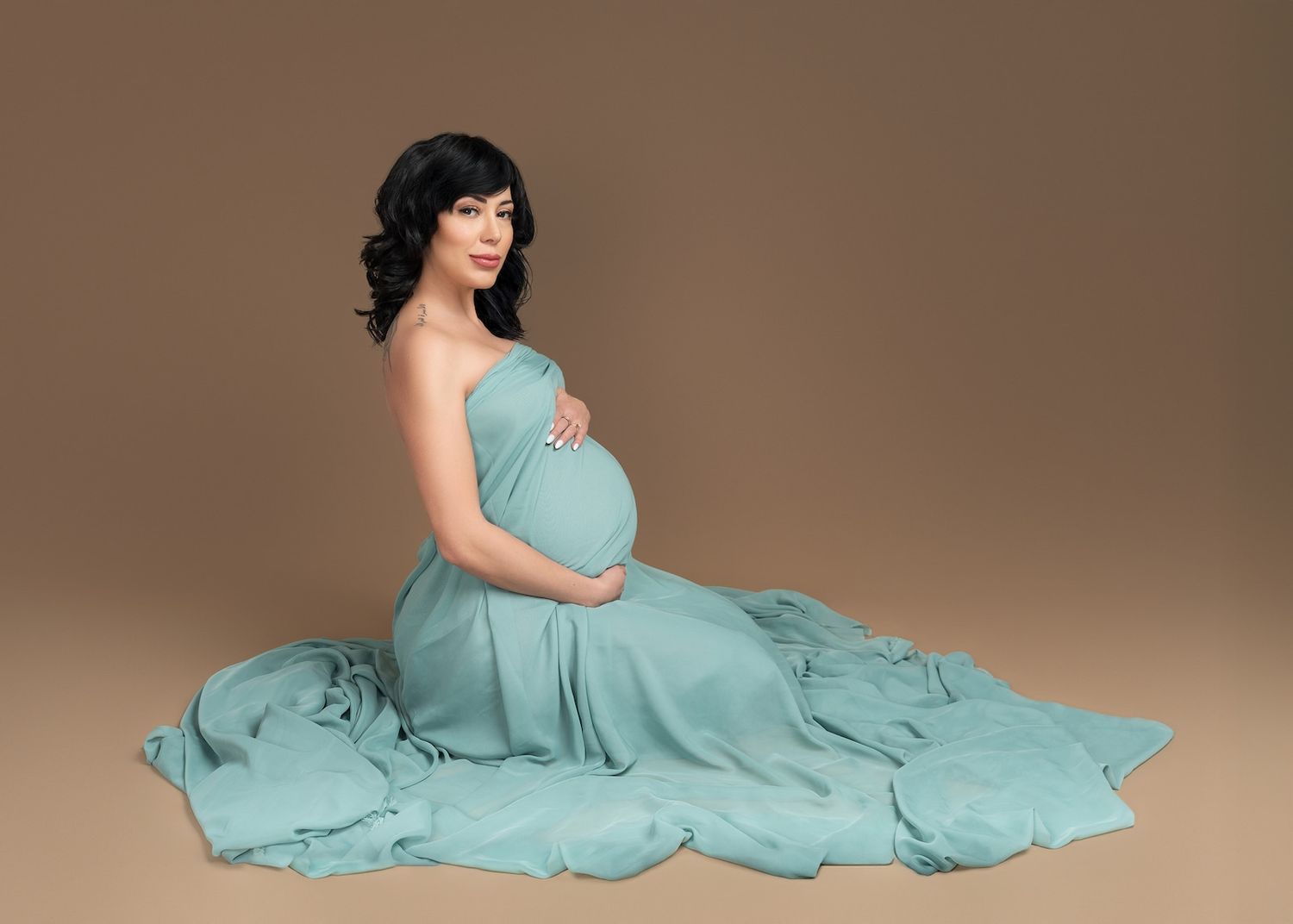 Denver maternity photography session of a mother gently holding her bump, draped in blue tulle in a private studio.