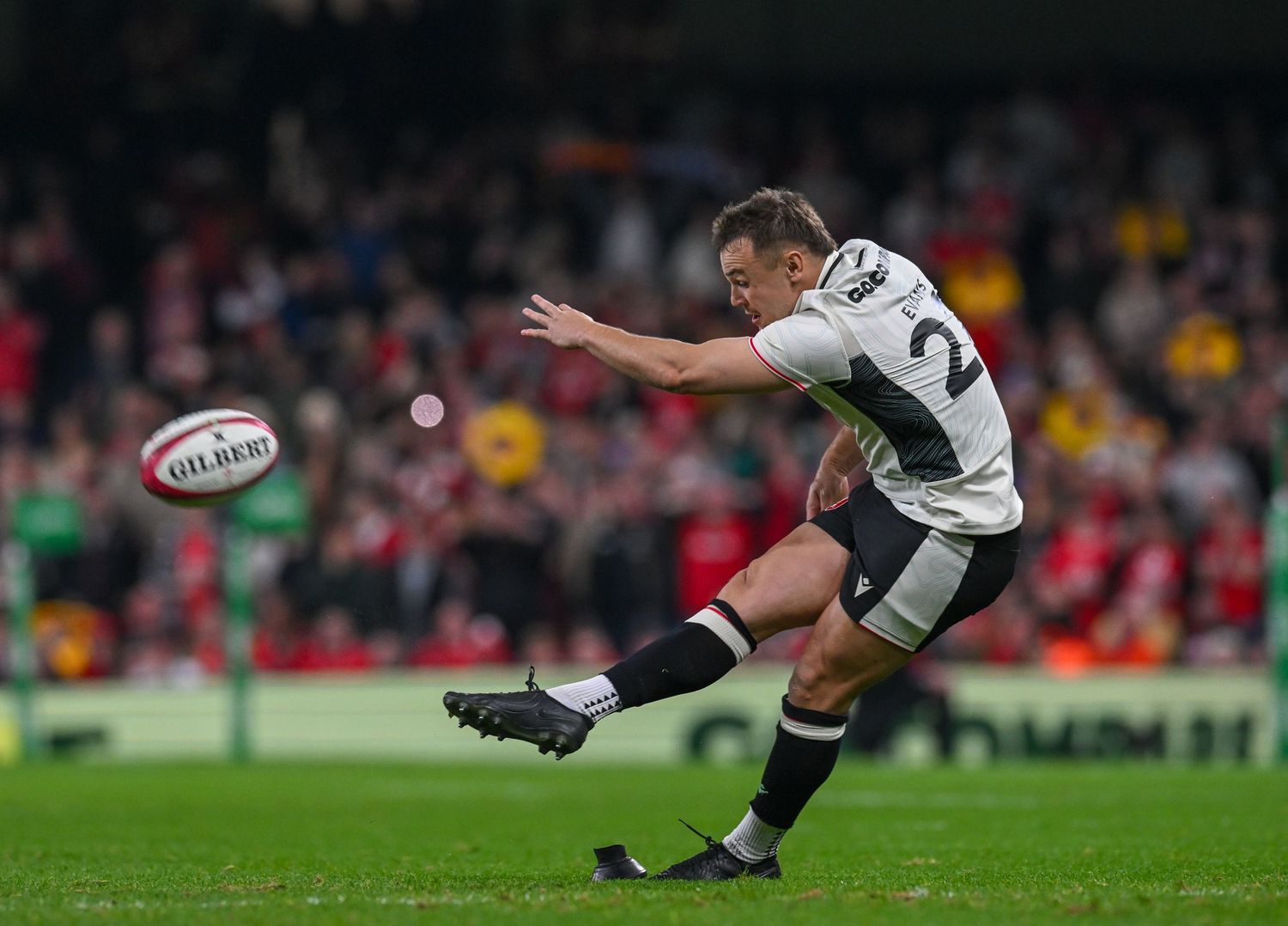 Rugby player in white jersey executes a kicking motion during match against red-uniformed team.