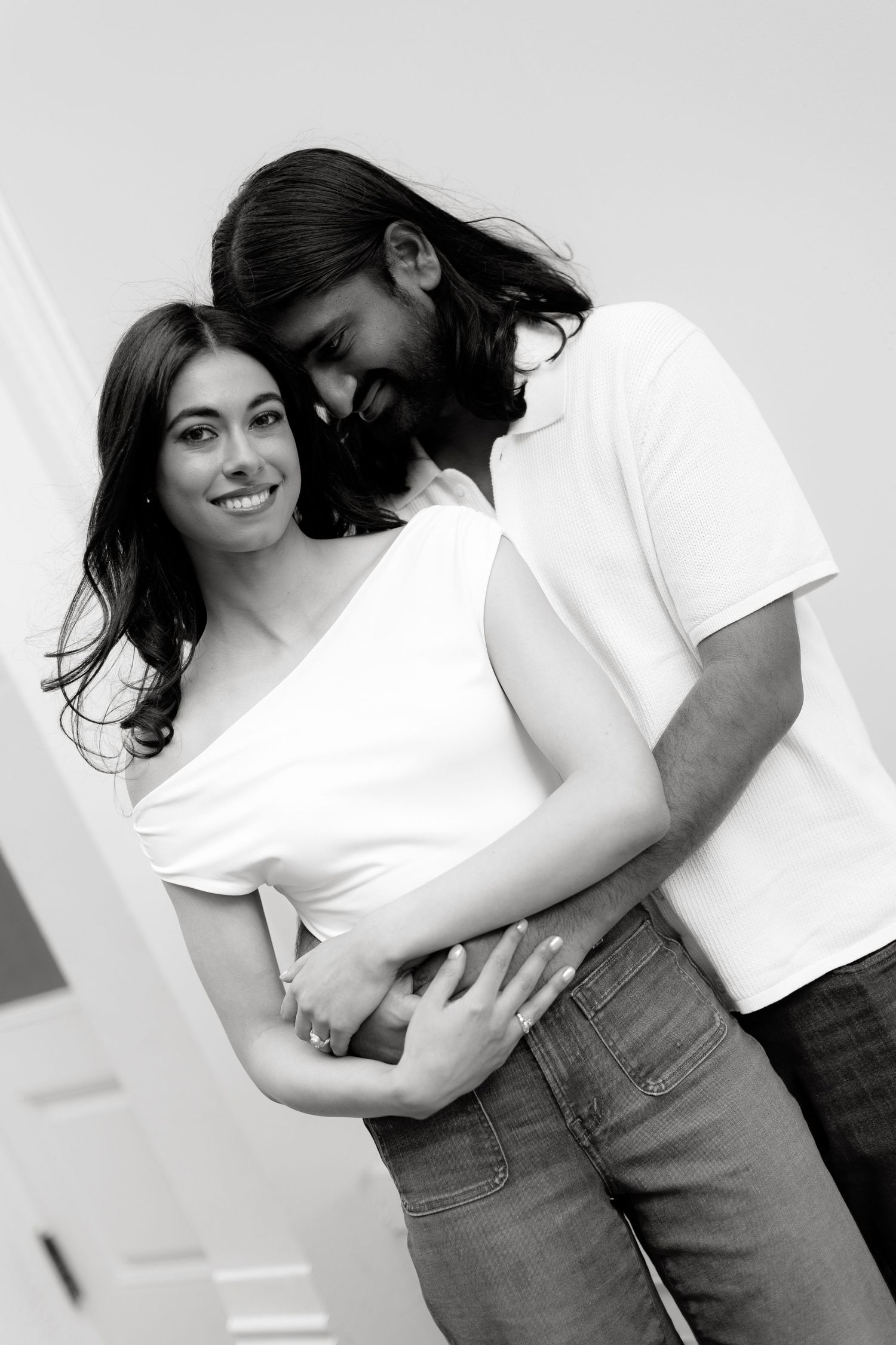 A romantic black and white portrait of a couple in white tops embracing and smiling together.