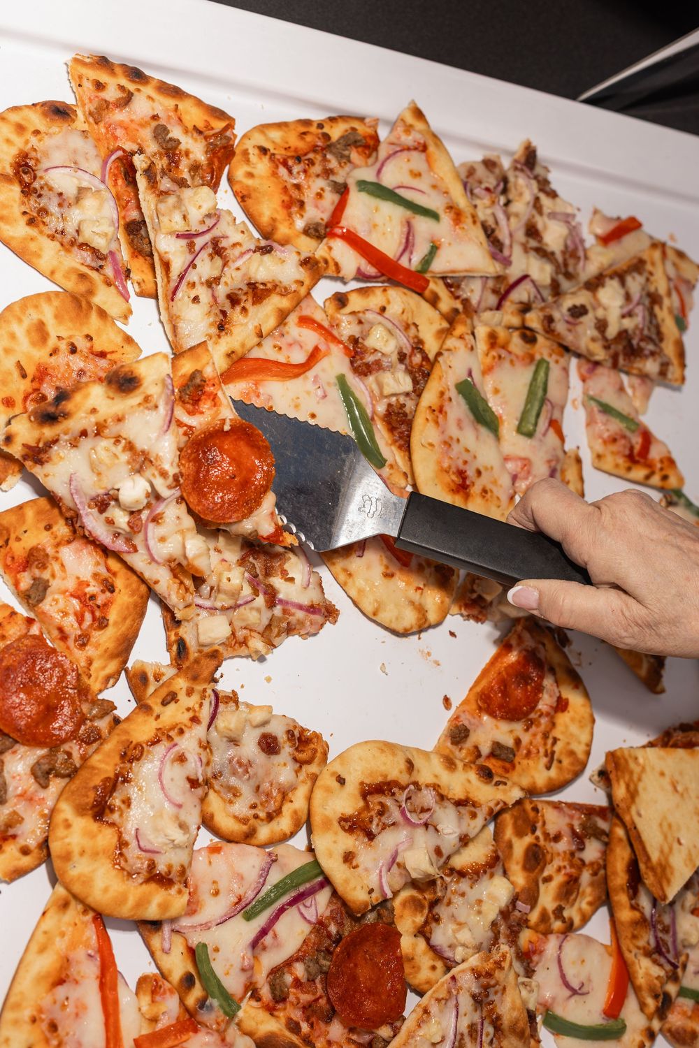 Sliced homemade pizza with pepperoni, mushrooms, red peppers and melted cheese being cut with a knife.