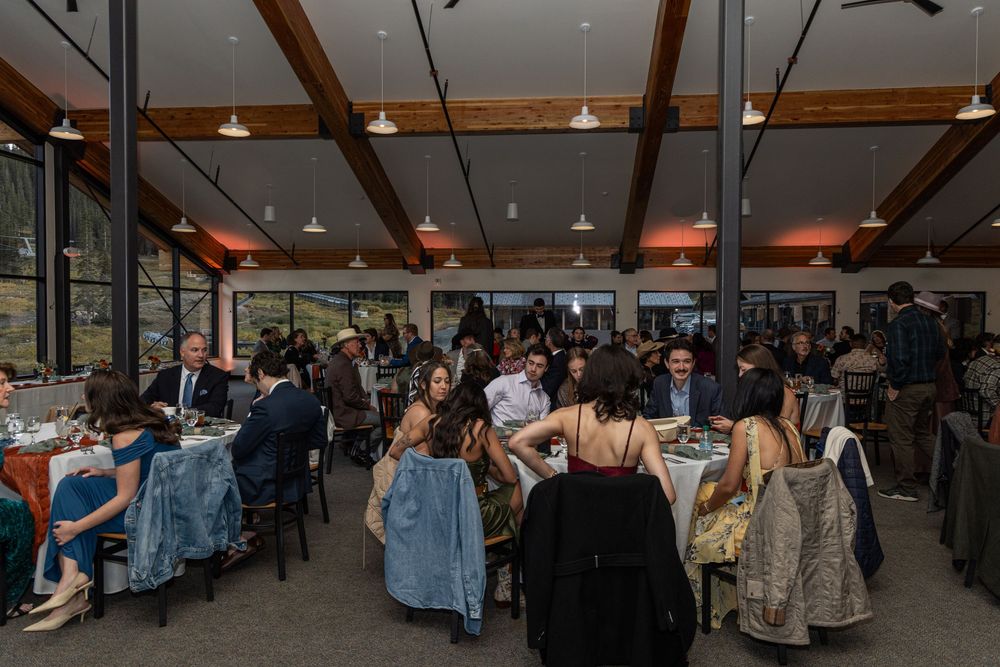 Crowd of people browsing vendor booths at an indoor market or craft fair with exposed wooden beams and lighting.