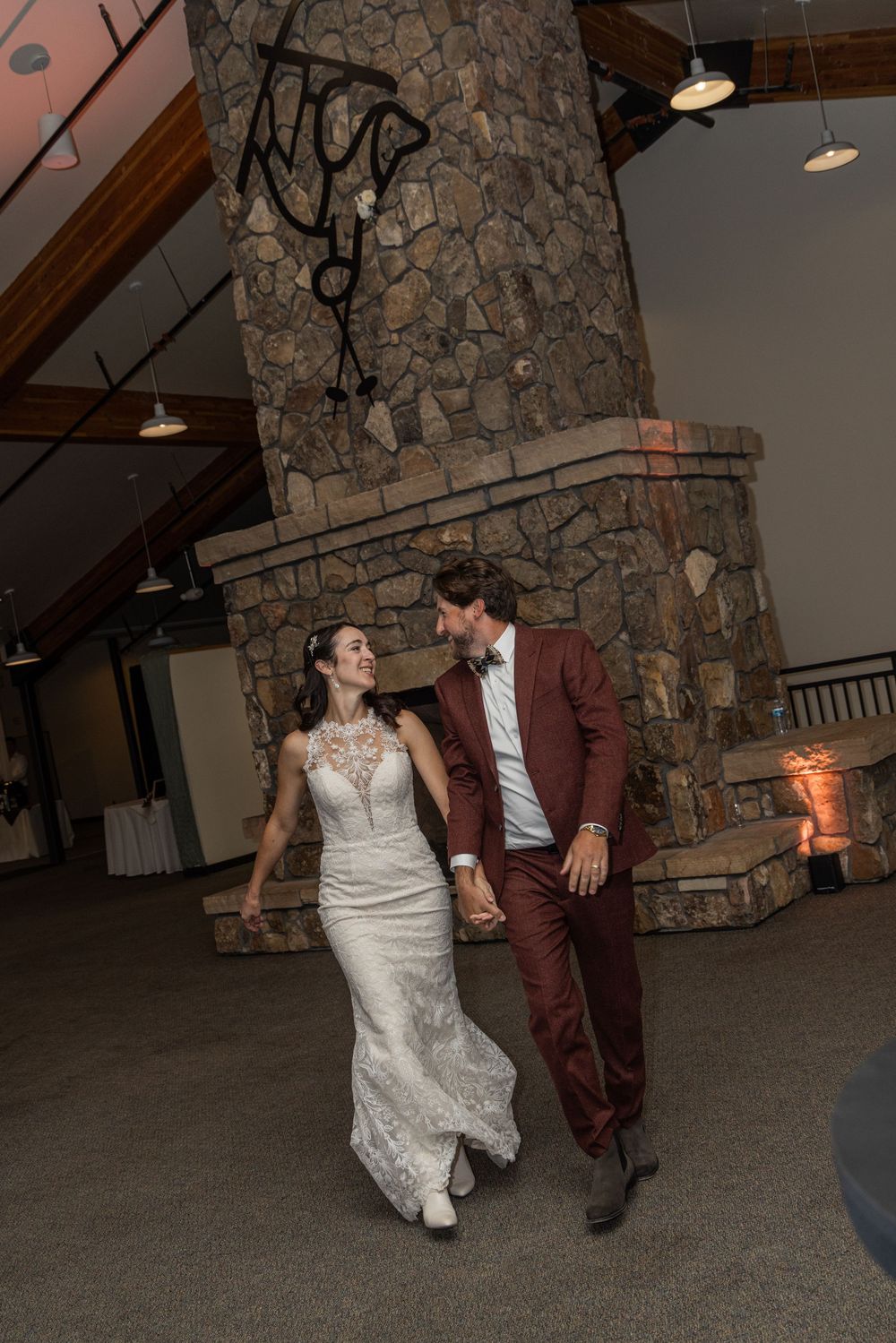 A couple in wedding attire dances together in front of a stone fireplace during their reception celebration.