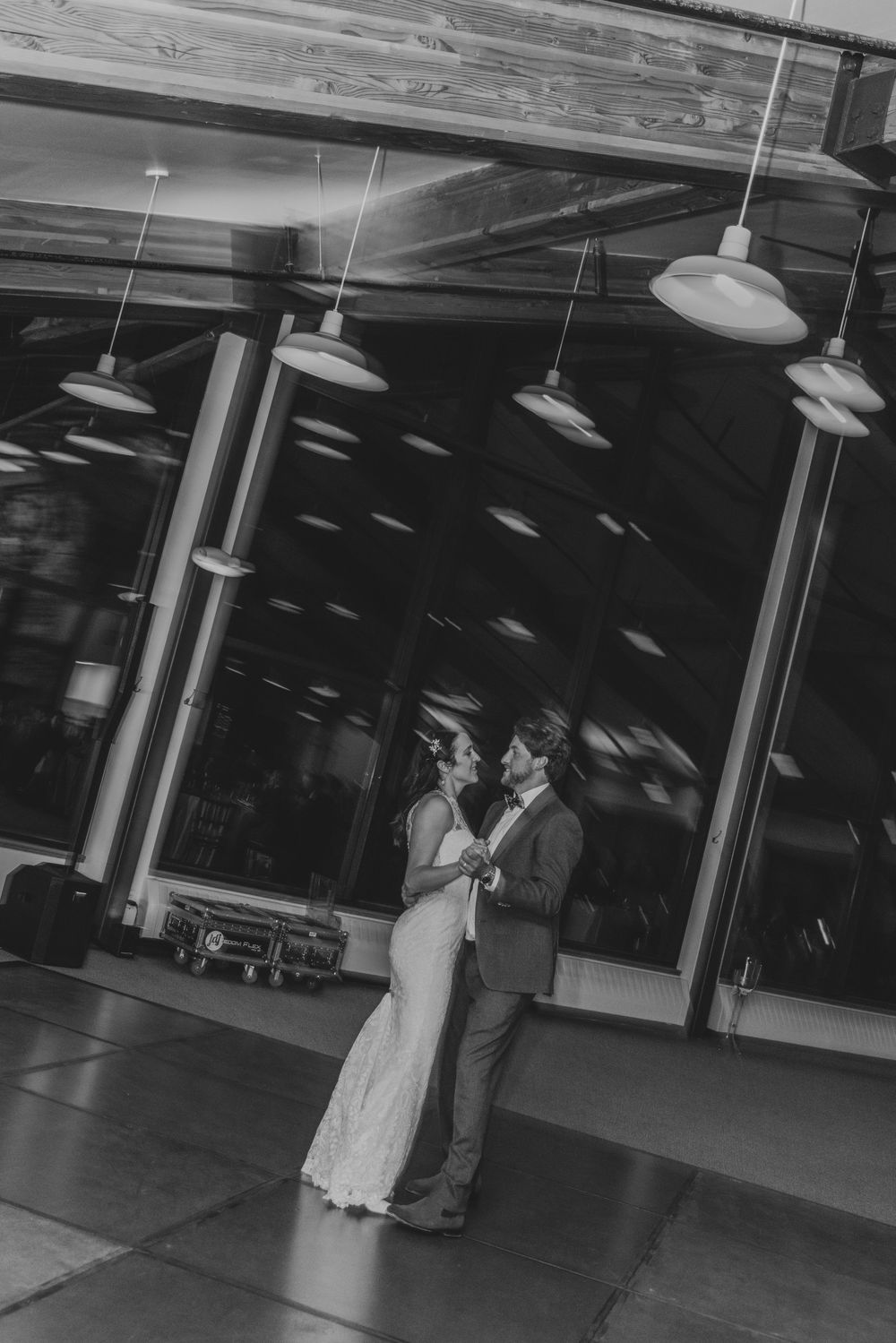 A couple shares a romantic dance moment under pendant lights in a black and white photograph.