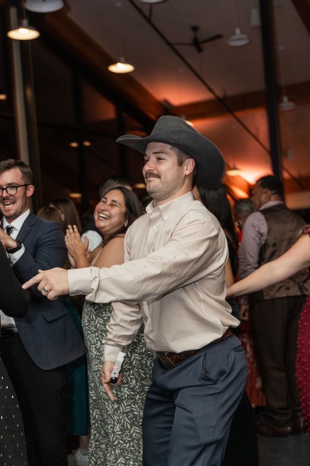 People dancing and celebrating at an indoor event with warm lighting and pendant lamps overhead.