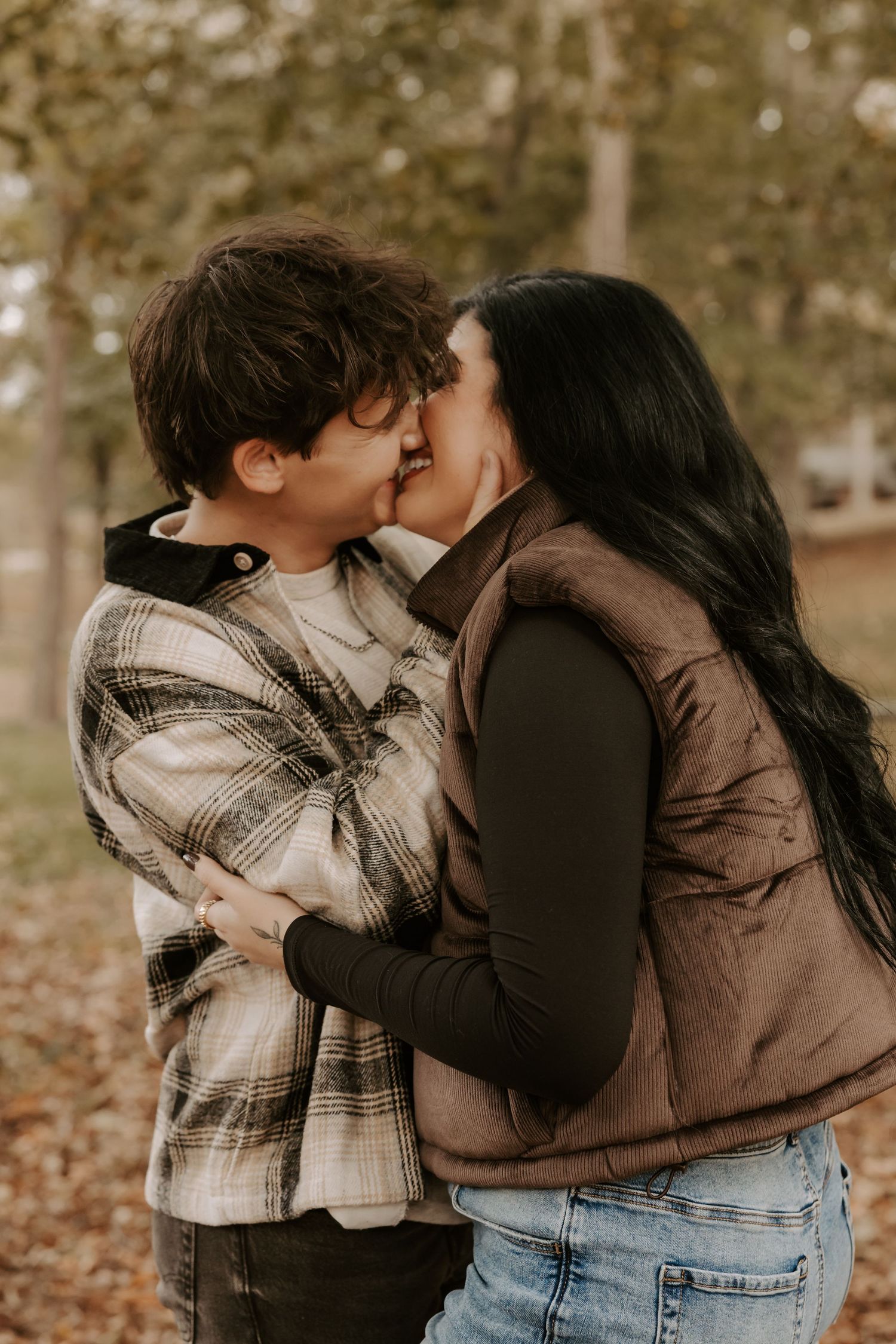 Romantic couple sharing a tender kiss in an autumn setting wearing casual outerwear.