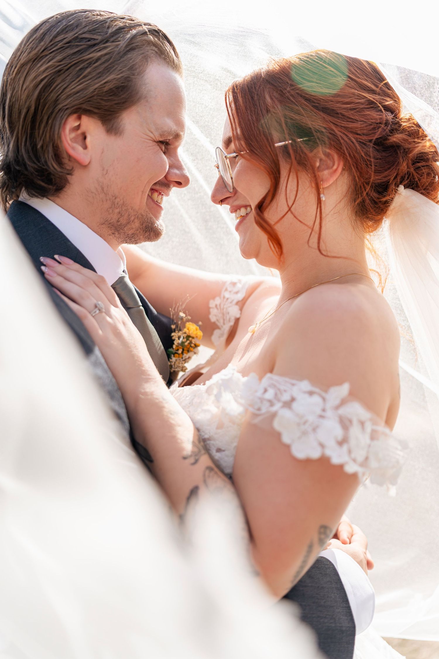 Romantic wedding couple sharing intimate moments in soft sunlight through a flowing white veil.