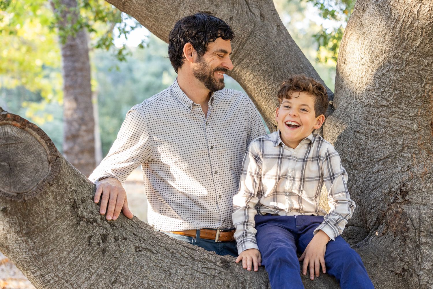 A parent and child share a laugh while sitting together on a large tree branch in Los Gatos.