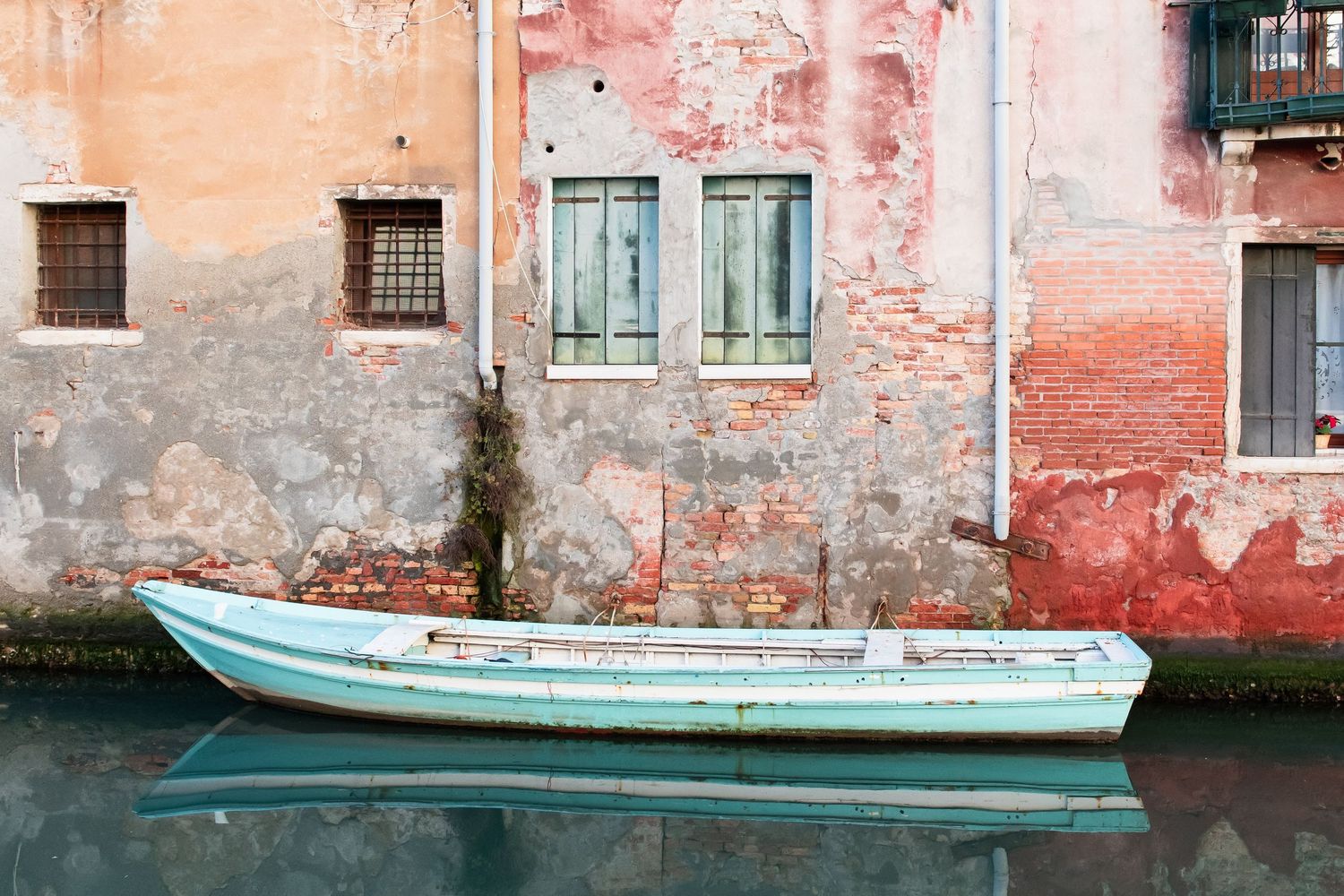 Mint green boat with a perfect reflection, floating in Venice in front and characterful and colourful houses