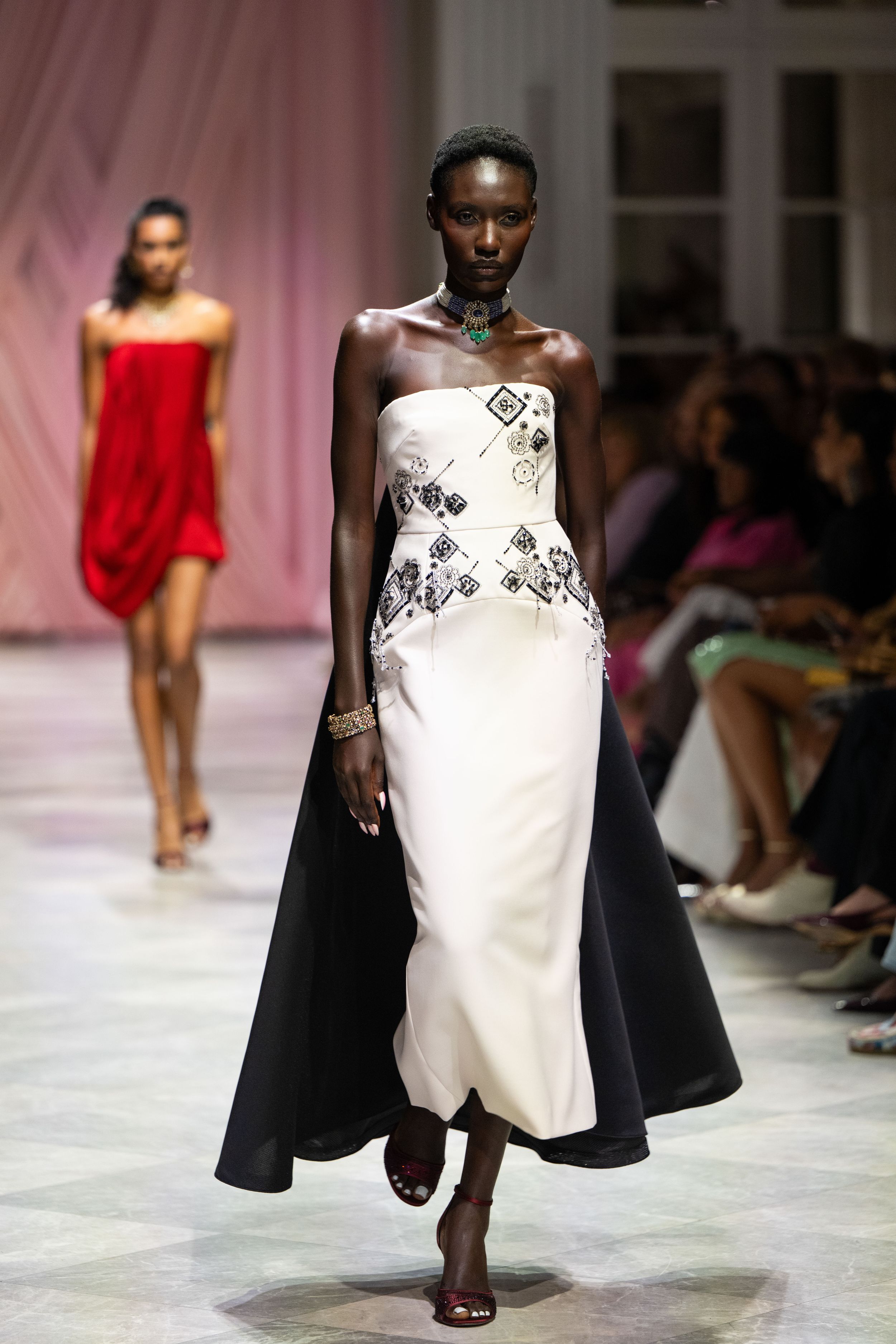 Models walk the runway in contrasting black and white evening wear with dramatic silhouettes at a fashion show.