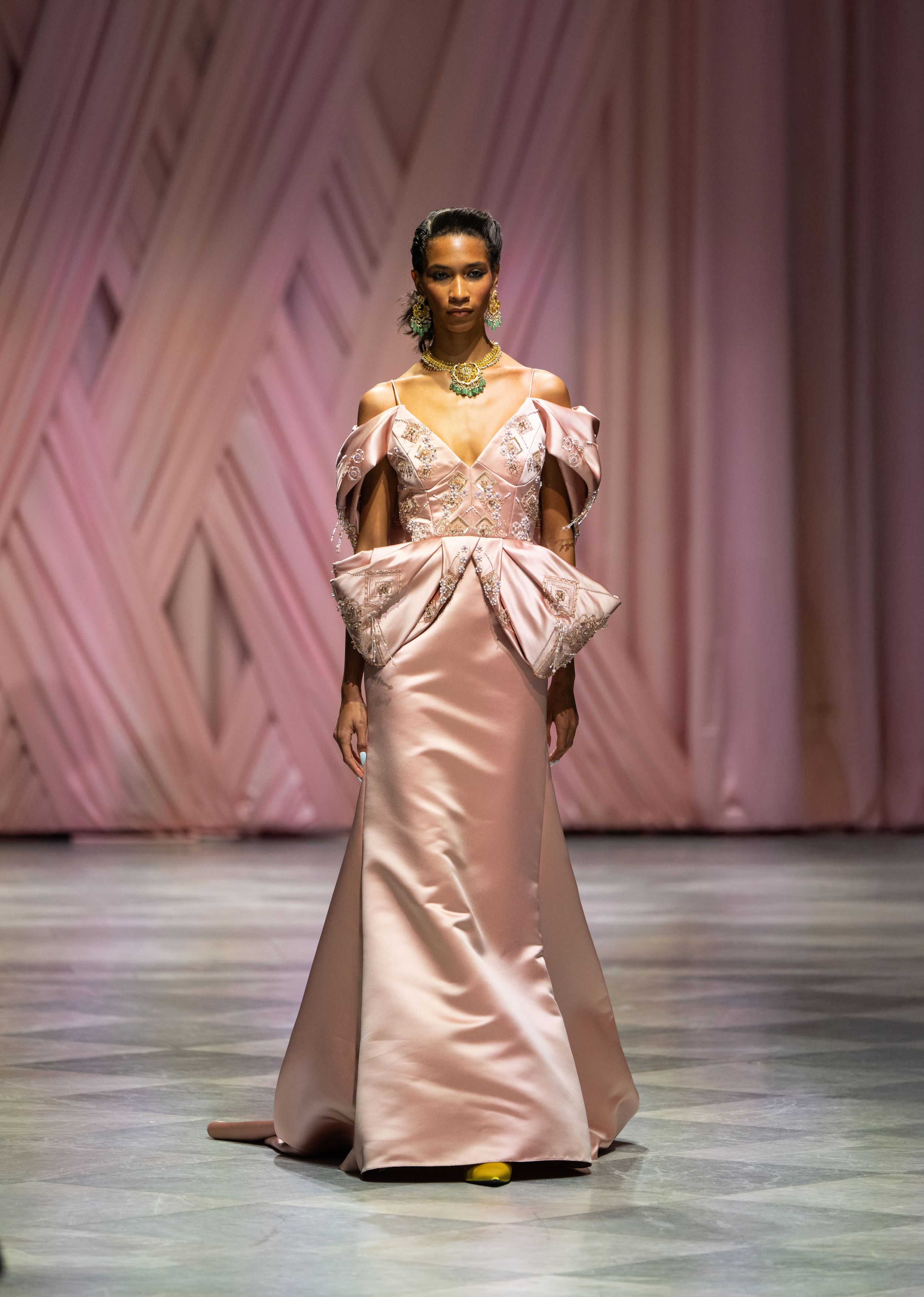 Elegant pink satin evening gown with dramatic off-shoulder puff sleeves and fitted silhouette on fashion runway.