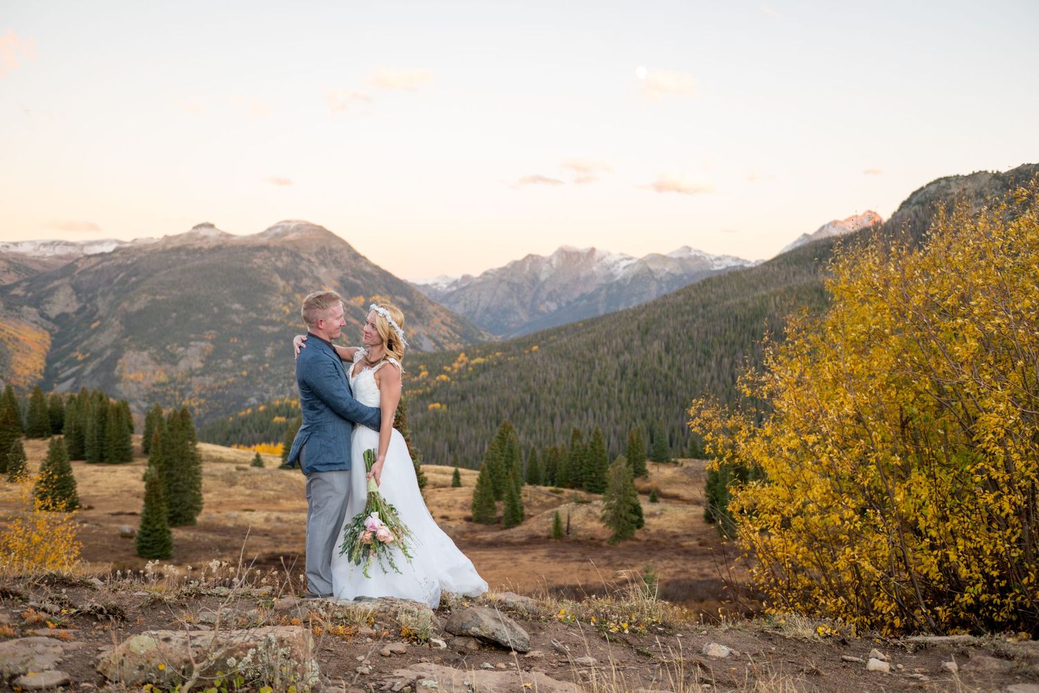 An eloping couple embraces during sunset in front of majestic mountain peaks of the San Juan mountains and golden autumn foliage.