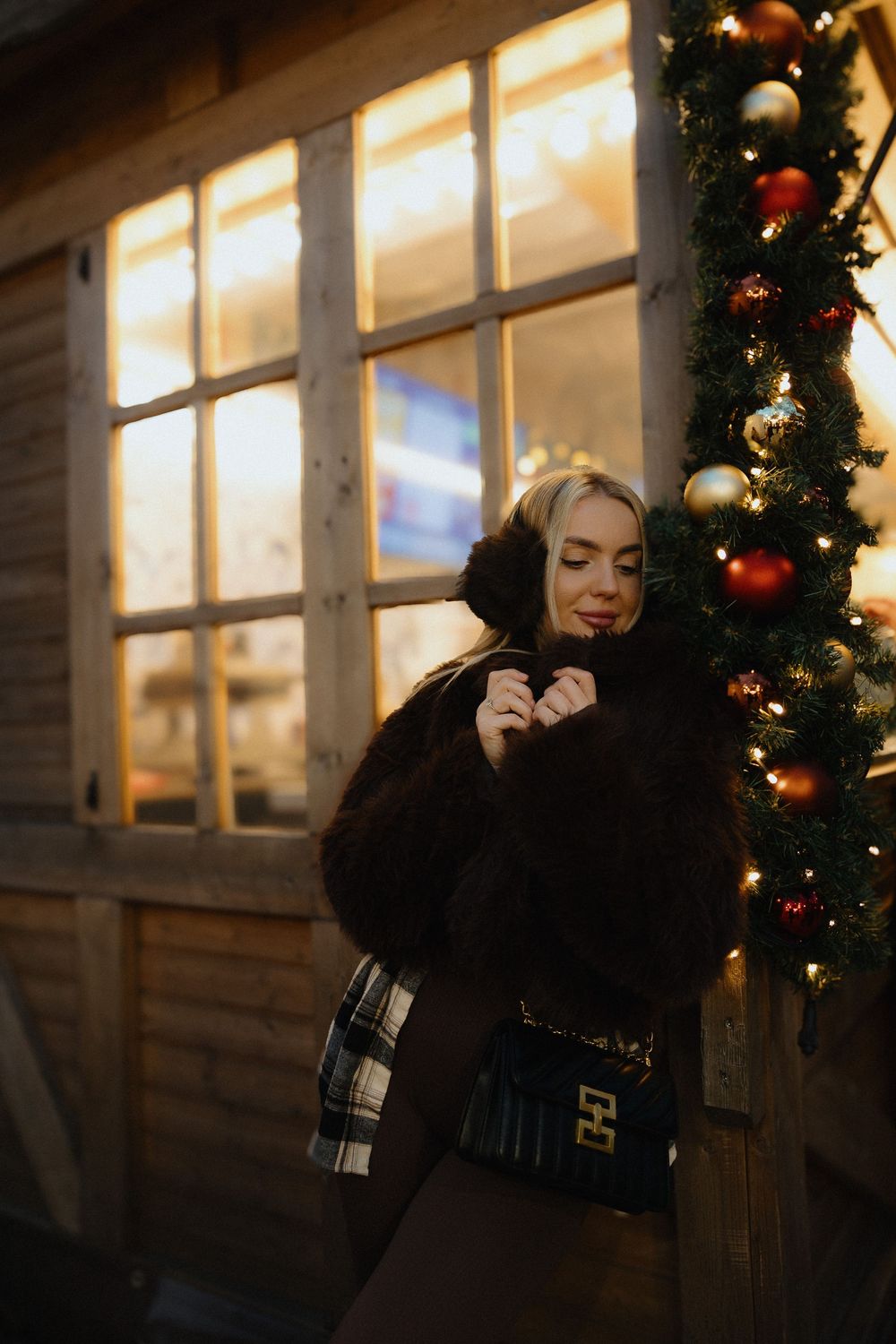 A festive winter scene with Christmas decorations and soft lighting against a wooden cabin exterior.