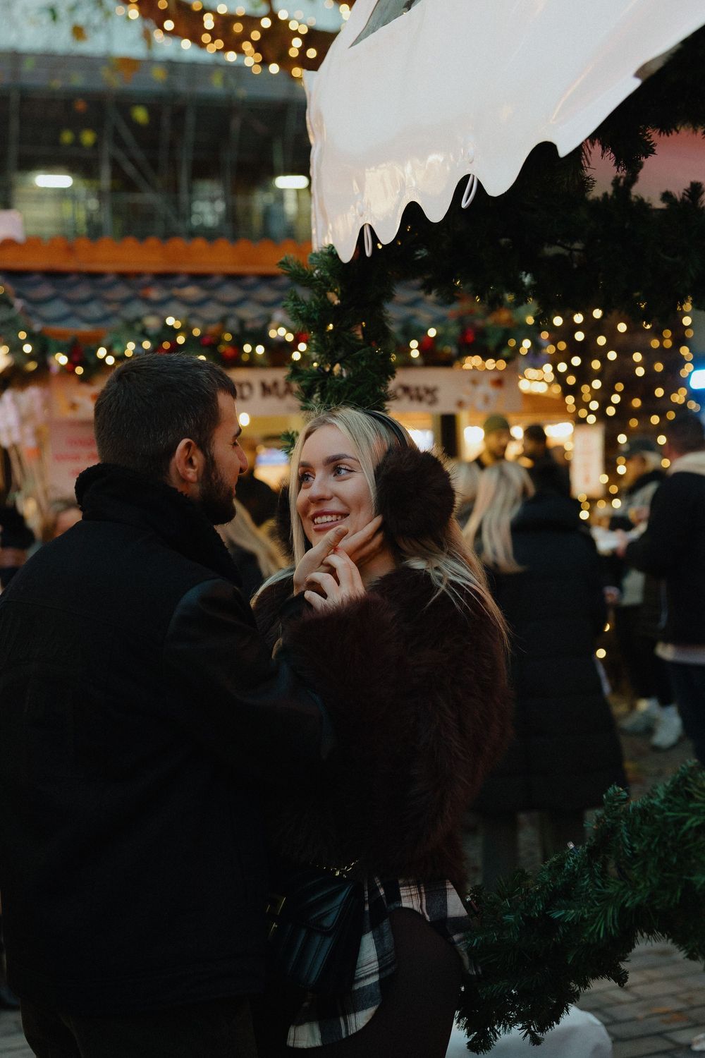 A couple shares a romantic moment under twinkling lights at an outdoor evening gathering.