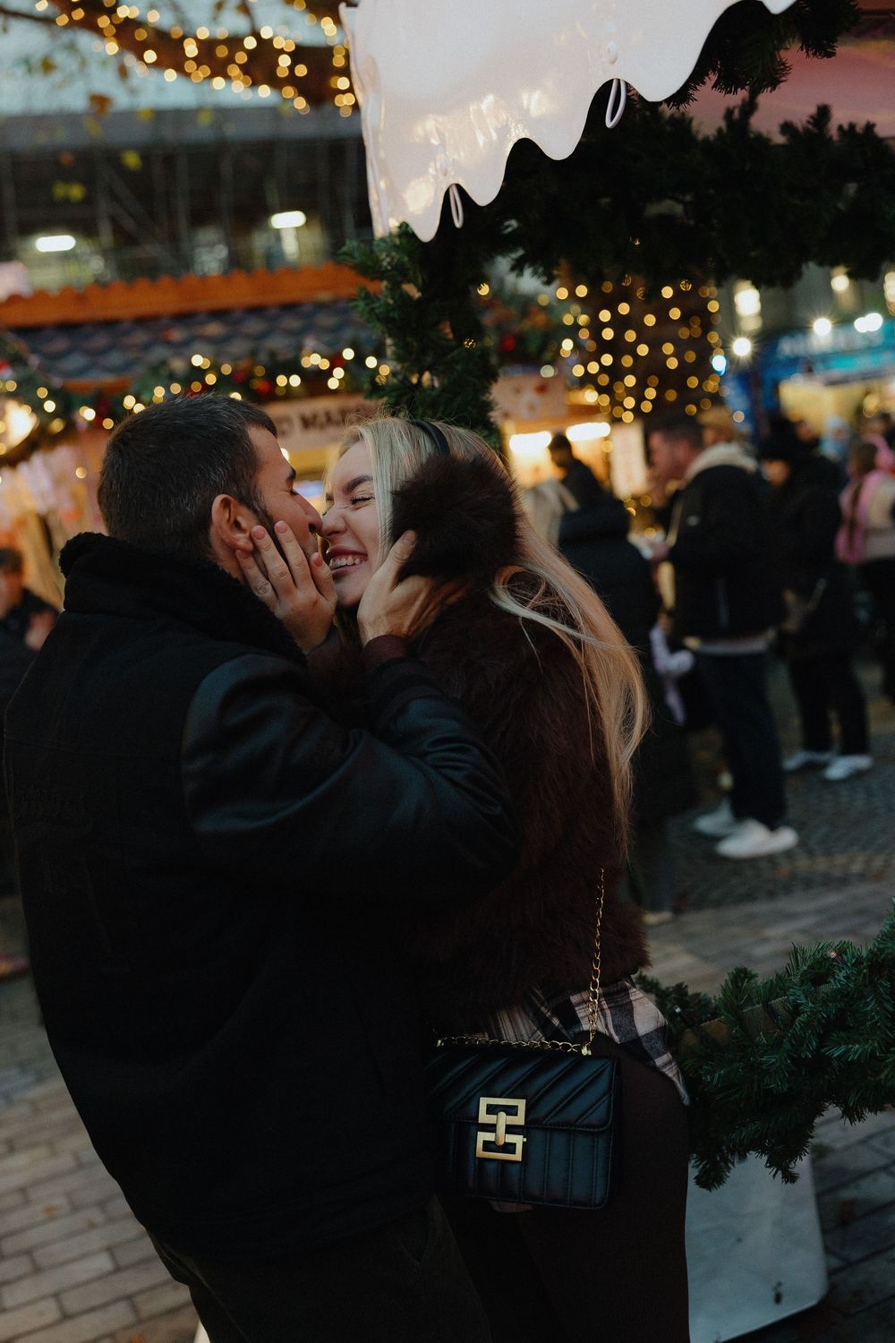 A romantic couple shares an intimate moment under twinkling string lights at dusk in an outdoor setting.