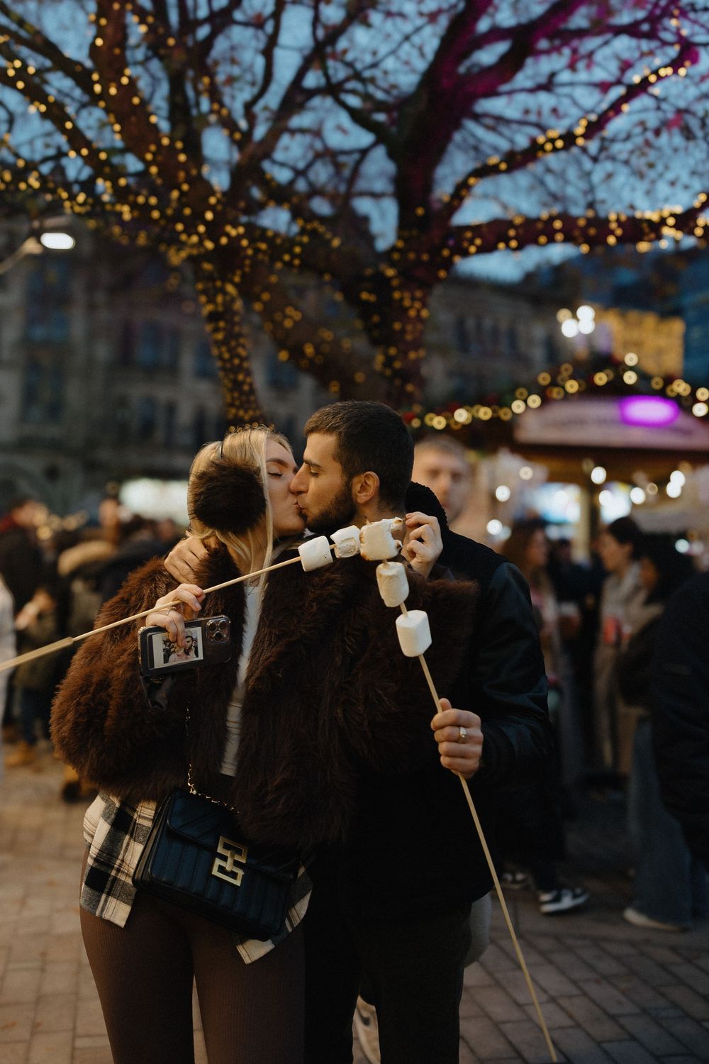 People playing a marshmallow string game at an outdoor evening event with twinkling lights in the background.