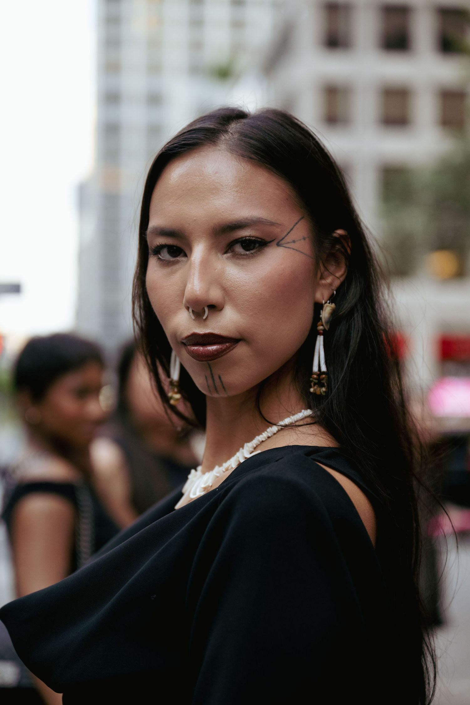 A person with long dark hair wearing black clothing poses in an artistic portrait series against a blurred background.