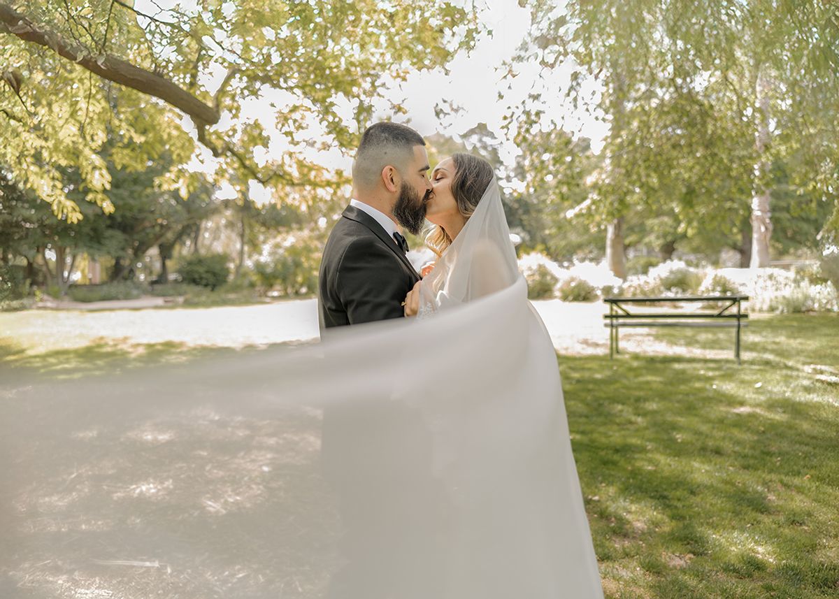 A couple in wedding attire walks together on a wooden boardwalk surrounded by trees and natural scenery.
