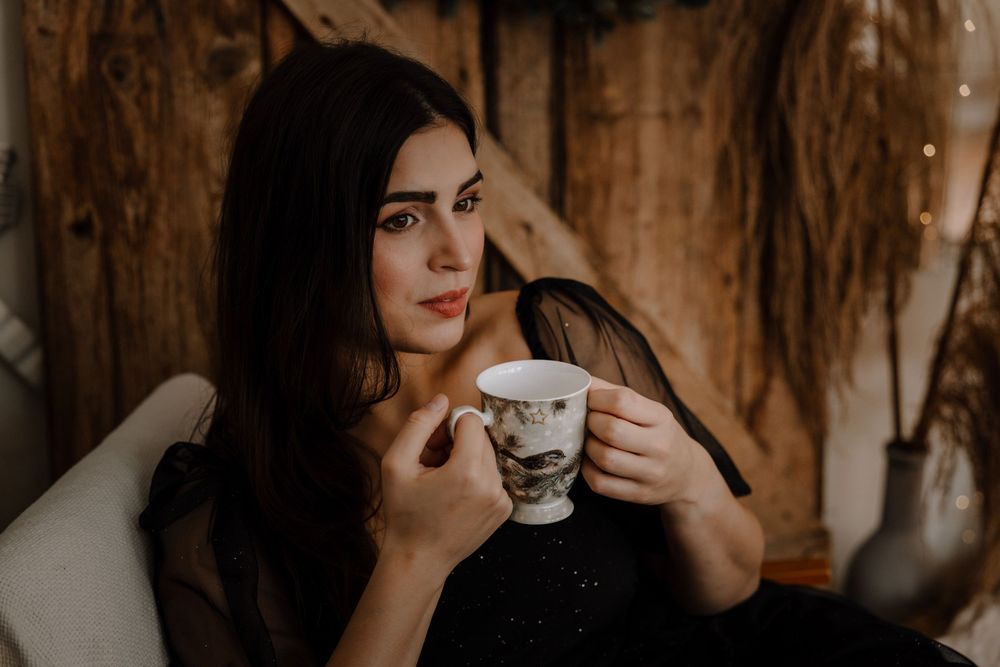 A person in a black sweater holds a white coffee cup against a rustic wooden wall background.