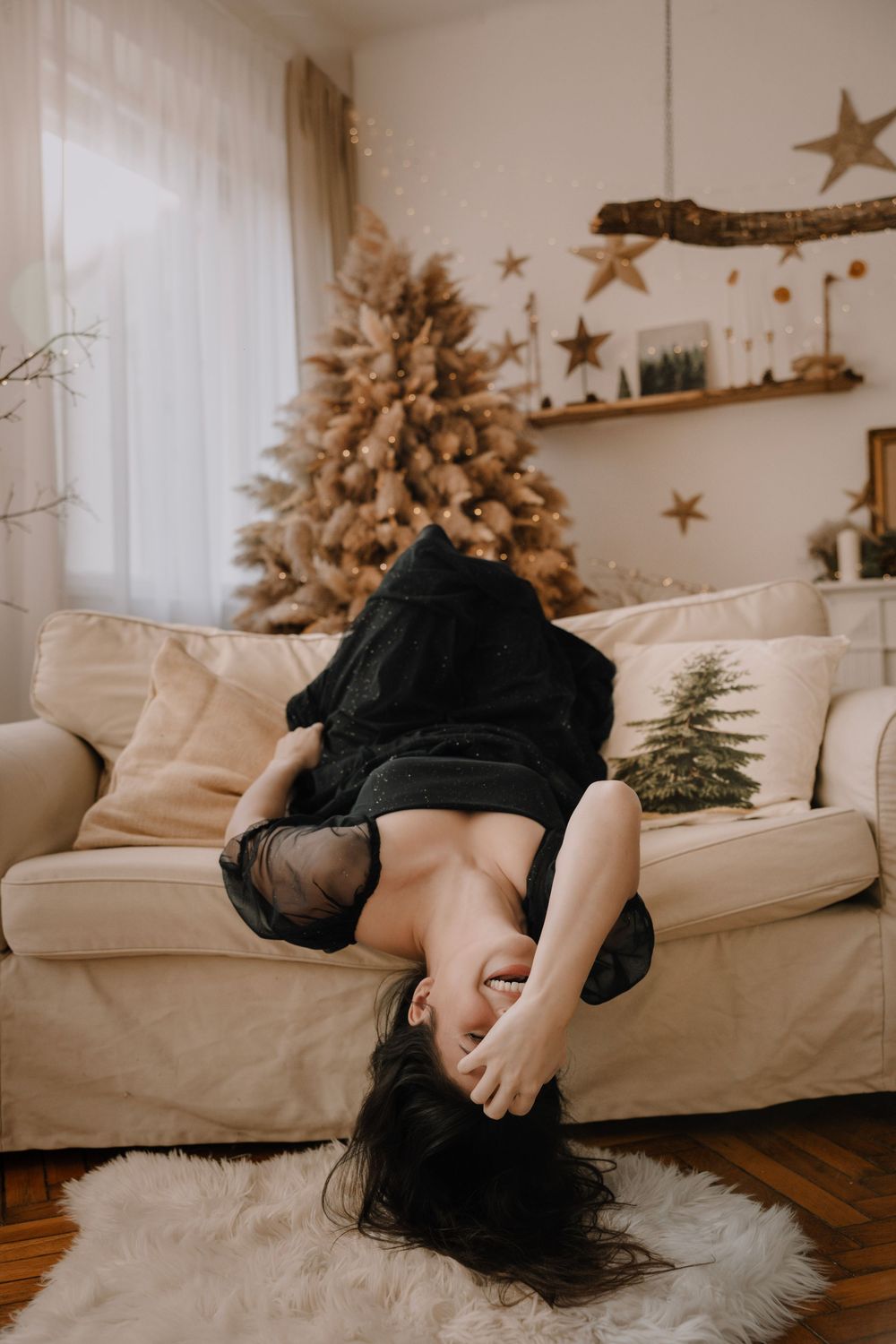 A person lying on a cream colored couch in front of a decorated Christmas tree with gold stars on the wall.