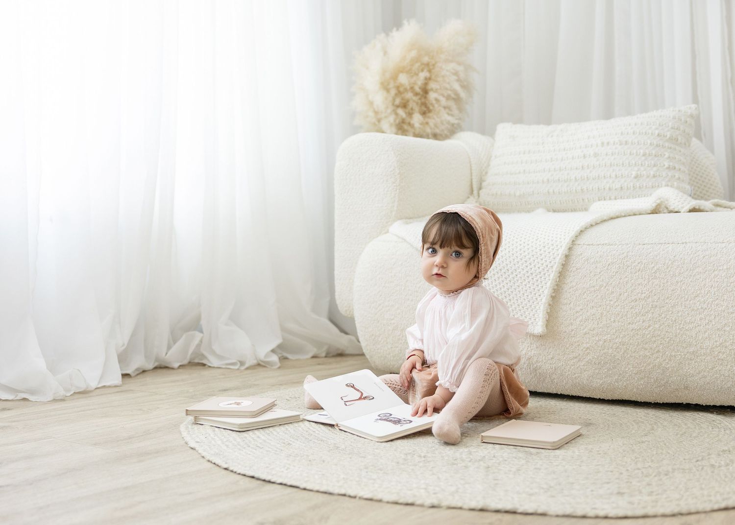Two children lying on white bedding while looking at a mobile device together.